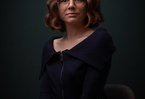 Ritratto di Simona Manganoni, donna con capelli ricci e occhiali, in posa seria.