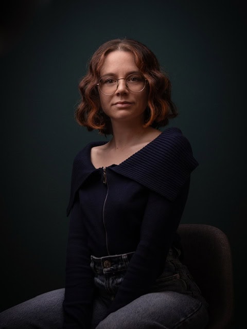 Ritratto di Simona Manganoni, donna con capelli ricci e occhiali, in posa seria.